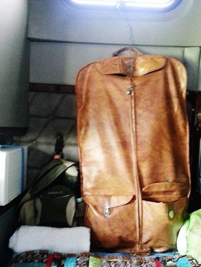 I tackled my clothing storage with a $3 hanging bag from the thrift store. The bag I got is an ancient American Tourist with the two pockets on one side and a big zipper space on the other. The hanger allows me to hook it into the window frame (where the metal is) and it hangs perfectly out of the way. My clothes stay separate from George’s and his Spartan wardrobe allows for me to stow the shower bags in the closet, instead of at the foot of the bunk. Again, it’s working great and I’m tickled to death.