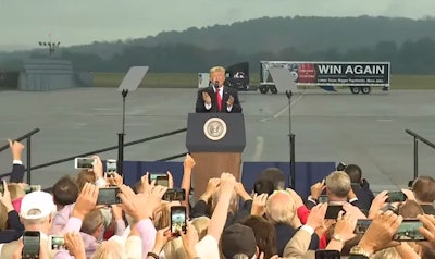 Trump spoke in front of a staged tractor-trailer. A message on the trailer read “Win again — Lower taxes. Bigger paychecks. More jobs.”