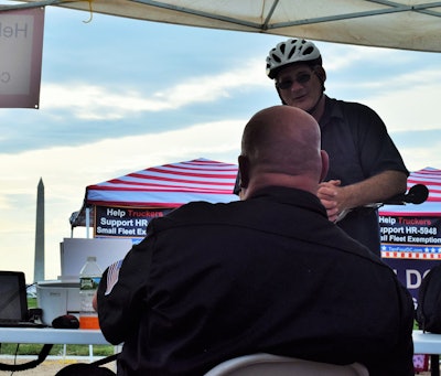 Owner-operator Doug Hasner talks to a member of the public in the central area of the 10-4 show on the National Mall Thursday-Saturday this past week. Note the sign referencing the H.R. 5948 ELD small fleet exemption bill in the background to the right of the cyclist.