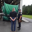 Truck driver and enforcement officer talking in front of truck being inspected