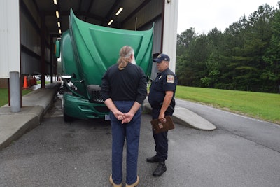 Truck driver and enforcement officer talking in front of truck being inspected