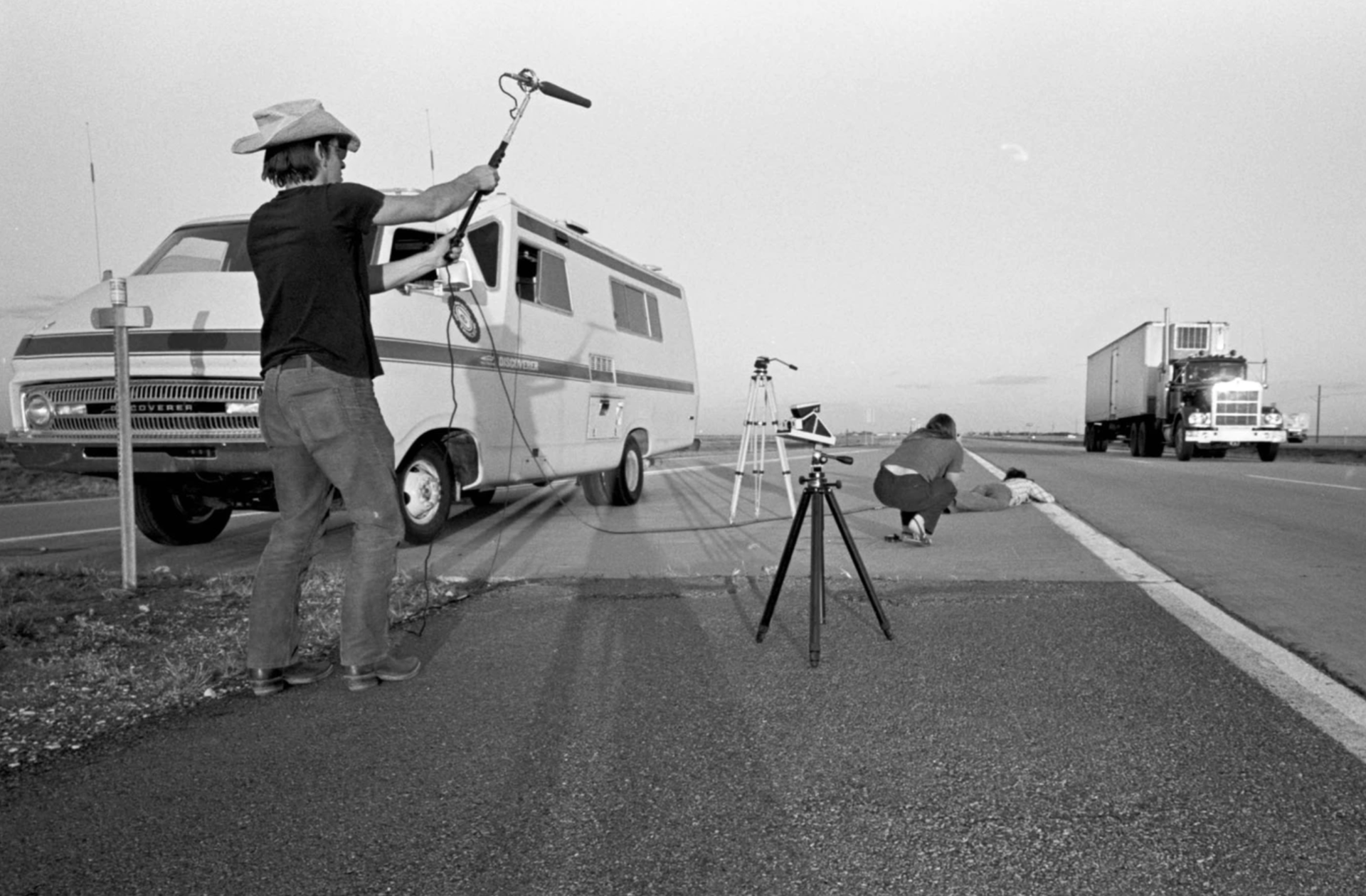 Video crew member on shoulder of highway filming truck