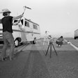 Video crew member on shoulder of highway filming truck