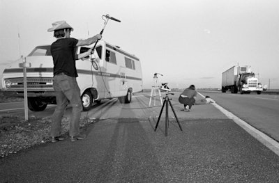Video crew member on shoulder of highway filming truck