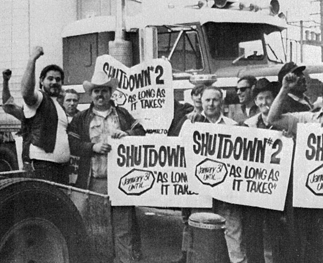 truck drivers in front of a semi-truck holding signs with the text shutdown #2 january 31 until as long as it takes on them
