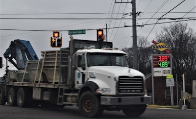 Semi-truck hauling a flat bed trailer through an intersection with a Sunoco gas and diesel sign in the background