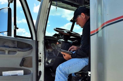 Owner-operator in driver's seat look at load board on tablet