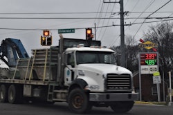 MACK truck with flatbed trailer passing in front of a sunoco gas station sign with regular gas price at $3.89 and diesel at $4.89