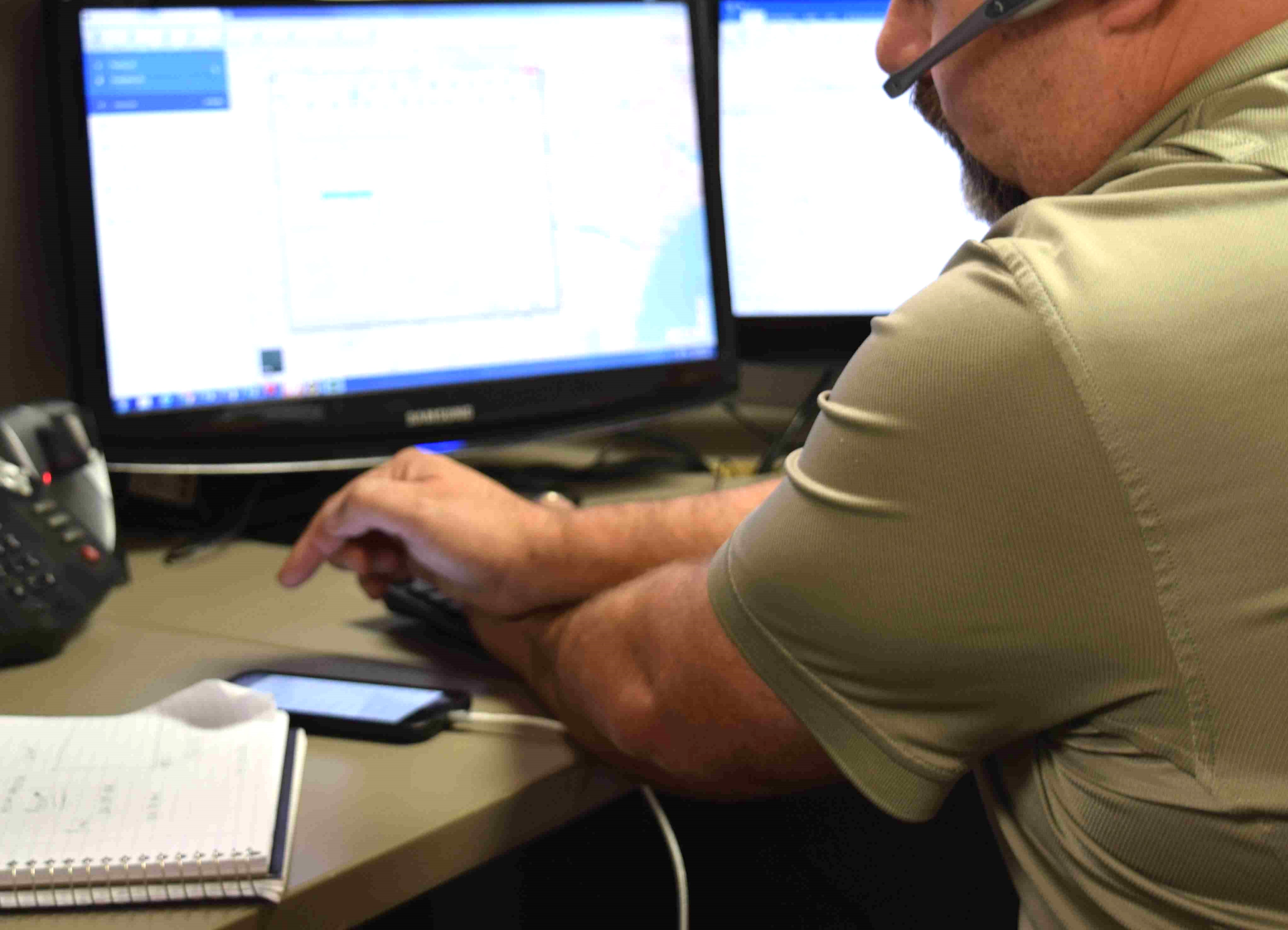 broker at desk looking at phone/computer terminal