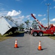 Red tow truck lifting a turned over semi-truck trailer