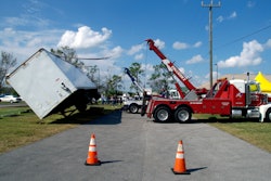 Red tow truck lifting a turned over semi-truck trailer