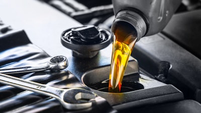 A bottle of engine oil being poured into an engine with a wrench nearby.