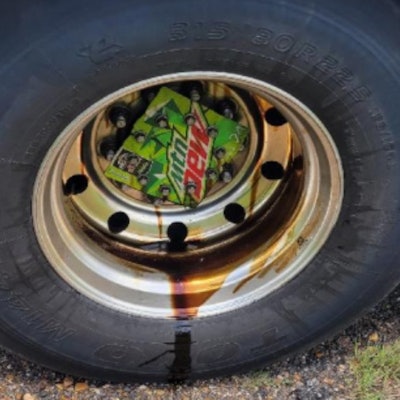 Semi-truck tire with part of a Mountain Dew box as a wheel cover allowing a wheel seal to leak oil,