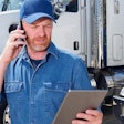 A man on the phone holding a tablet stands in front of trucks.