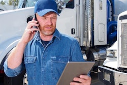 A man on the phone holding a tablet stands in front of trucks.