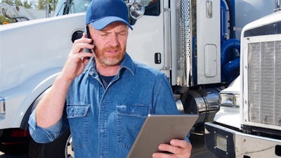 A man on the phone holding a tablet stands in front of trucks.