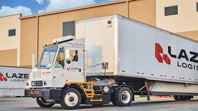 An Orange EV yard tractor hauling a Lazer Logistics trailer at a loading dock.