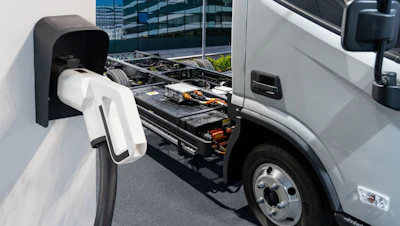 An unbranded battery-electric commercial truck is parked next to a charging station, revealing its exposed battery system.