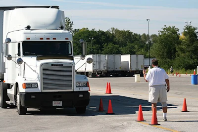 Commercial truck driver navigating around traffic cones during training exercise in parking lot