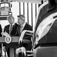 Three men in suits at podium with Presidential Seal during formal event with truck illustration backdrop