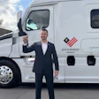 Professional man in dark suit holding truck door in front of white commercial vehicle with Keys to Progress branding