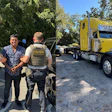 Police officers detain a man near a yellow commercial truck on a rural road.