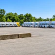 Fleet of commercial trucks and semi-trailers parked in organized rows at a logistics facility with trees in background