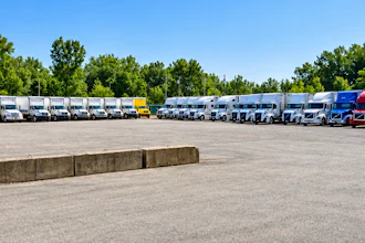 Fleet of commercial trucks and semi-trailers parked in organized rows at a logistics facility with trees in background