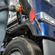 Worker refueling commercial truck with fuel pump nozzle at gas station