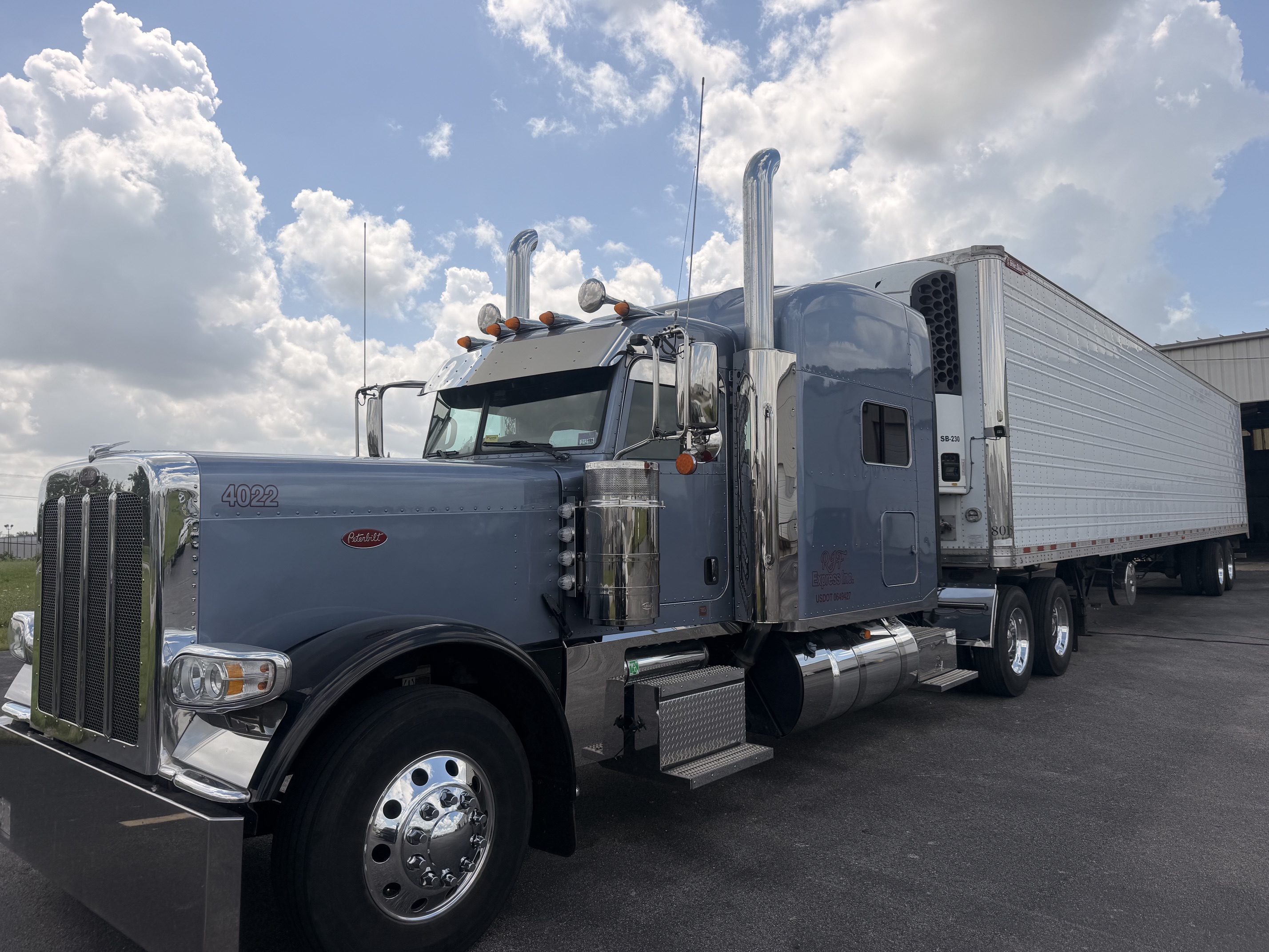 Gray Peterbilt semi-truck with white refrigerated trailer parked in lot under cloudy sky