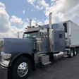 Gray Peterbilt semi-truck with white refrigerated trailer parked in lot under cloudy sky