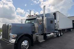 Gray Peterbilt semi-truck with white refrigerated trailer parked in lot under cloudy sky
