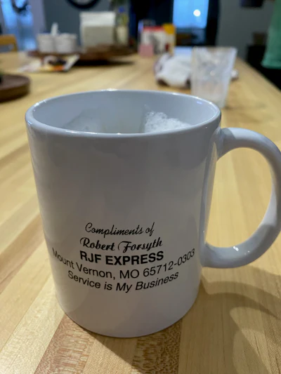White ceramic mug with RJF Express business information and tagline printed in black text