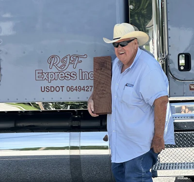 Smiling man in cowboy hat holding wooden plaque next to RJF Express Inc commercial truck