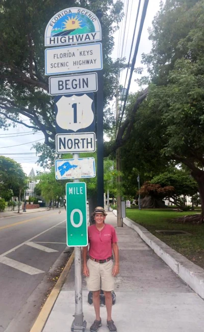 Man in pink shirt posing at Mile 0 marker of Florida Keys Scenic Highway on US Route 1 North
