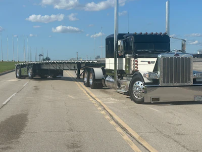 Black and white Peterbilt semi-truck with flatbed trailer on highway under blue sky