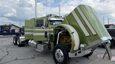 Vintage green and white Peterbilt semi-truck with tilted cab on display in industrial yard