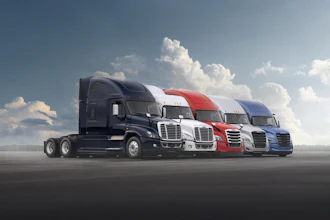 Row of five commercial semi-trucks in navy, white, red, and blue colors parked on asphalt against a cloudy sky
