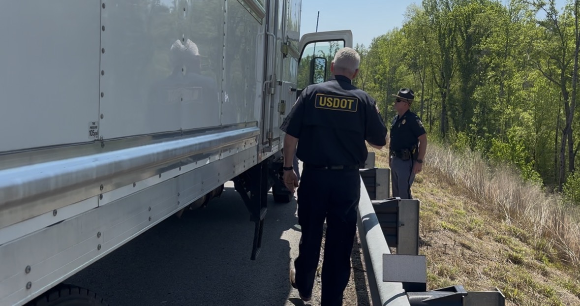 USDOT officials inspect a commercial truck on a rural roadside with trees in background