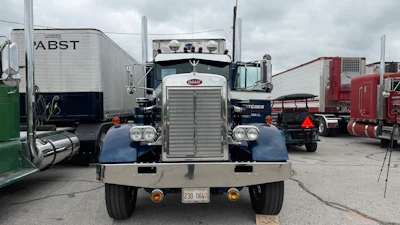 Front view of a classic Peterbilt semi-truck with navy blue cab and chrome details parked among other commercial vehicles
