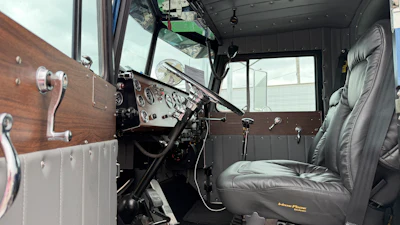 Restored vintage truck interior with wood-paneled dashboard, leather seat, and steering wheel