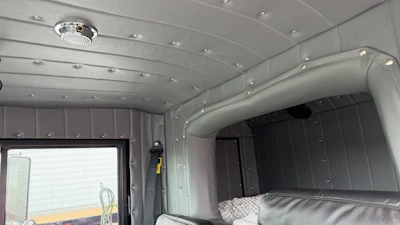 Modern RV interior with silver aluminum walls, recessed ceiling lights, storage compartments, and cushioned seating area