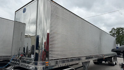 Silver refrigerated semi-trailer truck parked outdoors with horizontal ribbed sides and red trim details