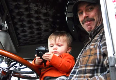 Adult man and toddler in orange shirt sitting in vehicle cabin, child holding radio microphone