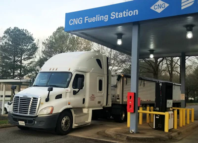 White Freightliner semi-truck refueling at CNG fueling station with blue canopy and yellow safety bollards