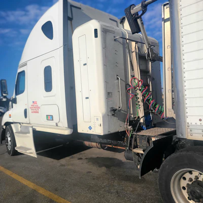 White commercial truck cab connected to trailer with exposed wiring and electrical components visible in daylight parking area