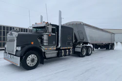 Black Peterbilt semi-truck with silver grain trailer parked in snowy industrial lot