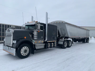 Black Peterbilt semi-truck with silver grain trailer parked in snowy industrial lot