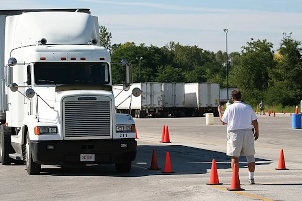 White Freightliner semi-truck navigating traffic cones during driver training course in parking lot