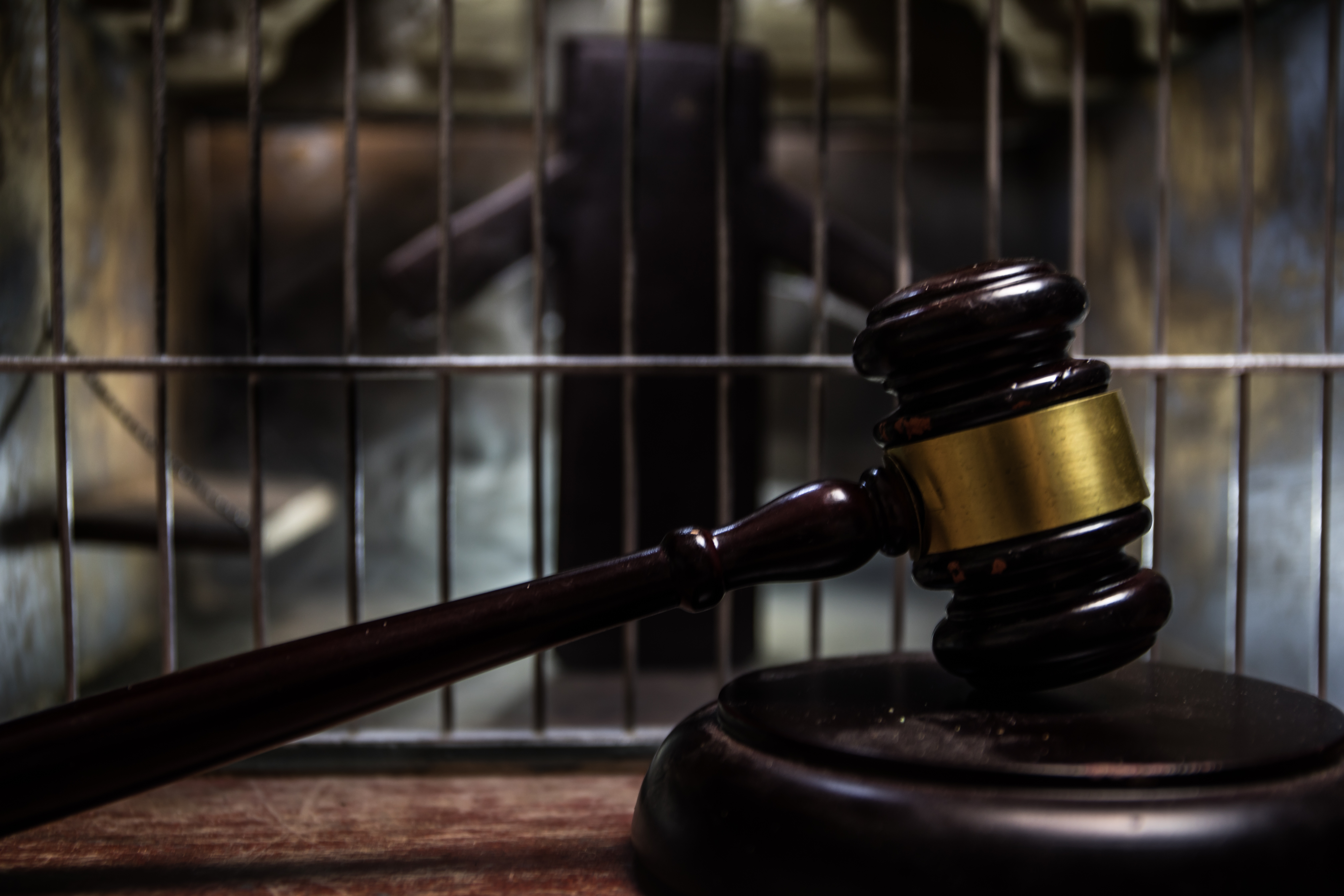 Judge's gavel on wooden block with prison cell bars in background symbolizing law and justice
